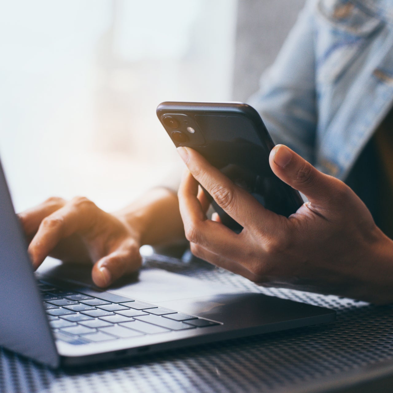 A woman using a computer and mobile phone at a workspace.