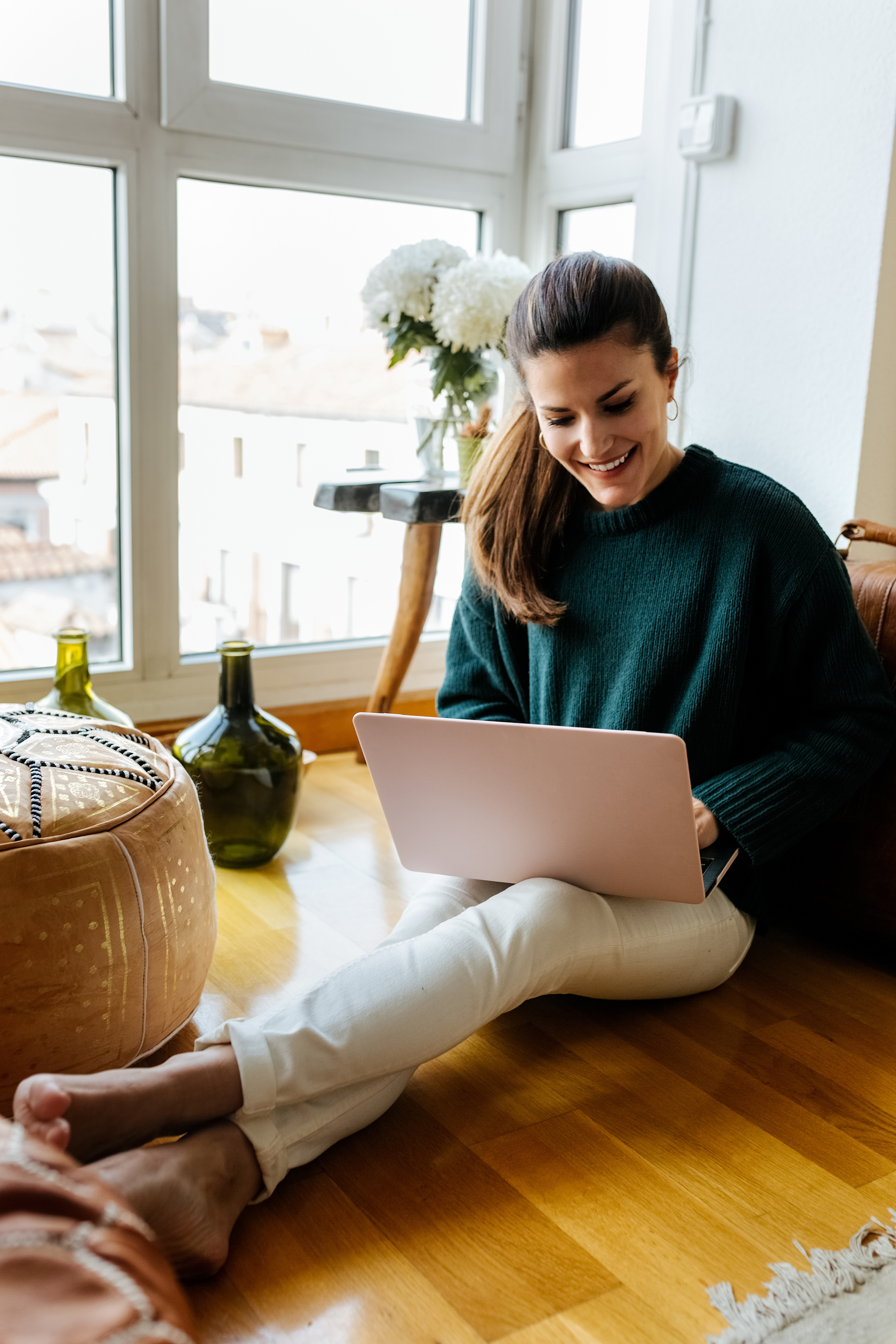 A young woman is seen happily working on her laptop. From the background it appears that she is at her home.