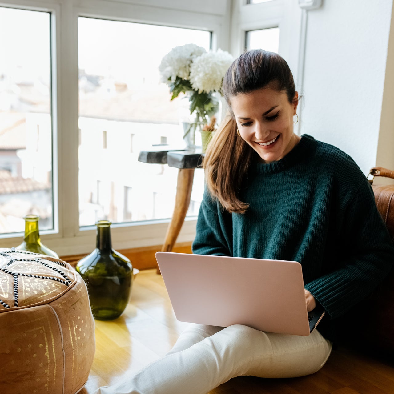 A young woman is seen happily working on her laptop. From the background it appears that she is at her home.