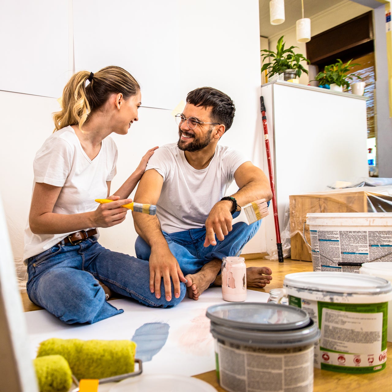 A young couple sitting on the floor, seemingly taking a break from painting a room.