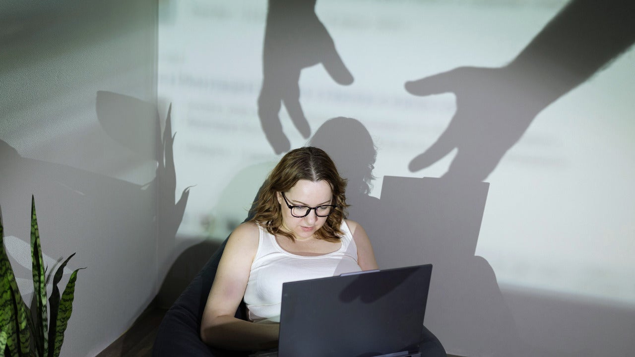 Image illustrating a set of shadow hands coming down on top of a person's laptop