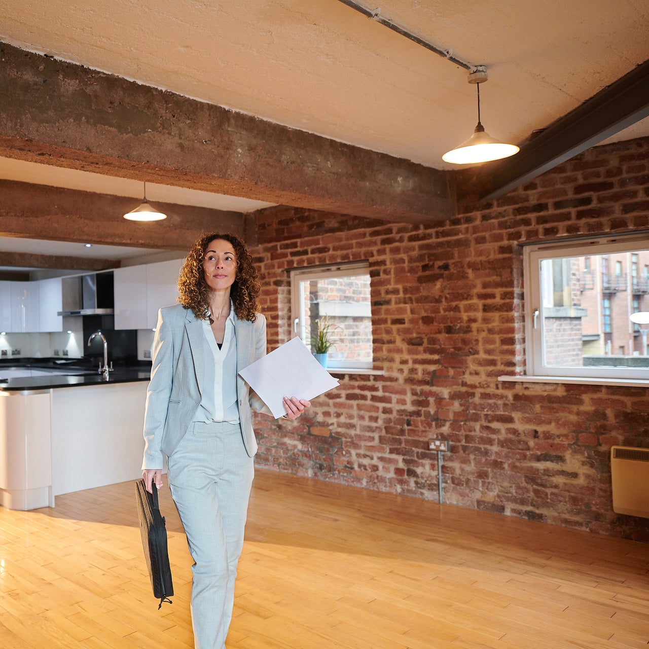 A confident woman wearing corporate suit is displaying a satisfactory smile while walking, carrying some papers and a laptop bag.