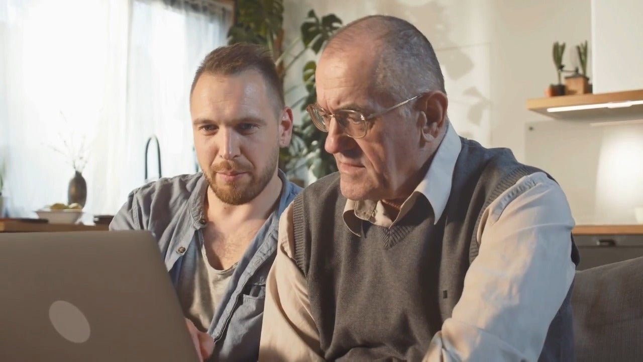 A younger man helping an older man with a laptop