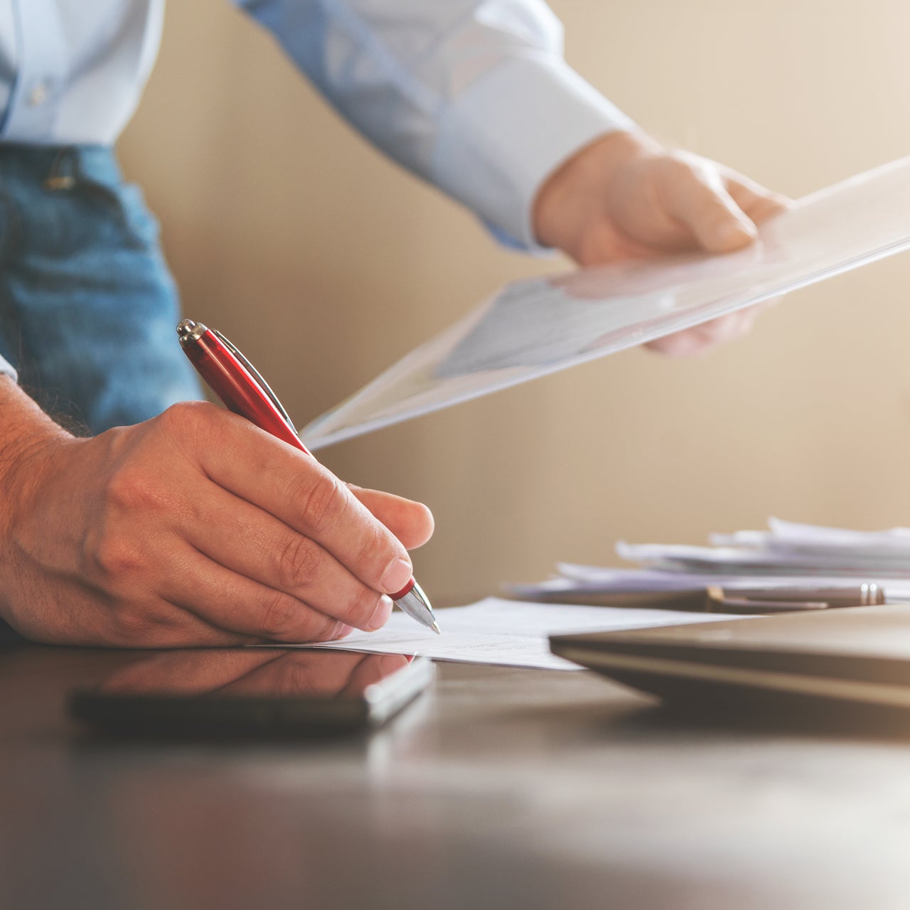 A professional in formal attire holding a pen and some paper. Only his hands are visible in the picture.