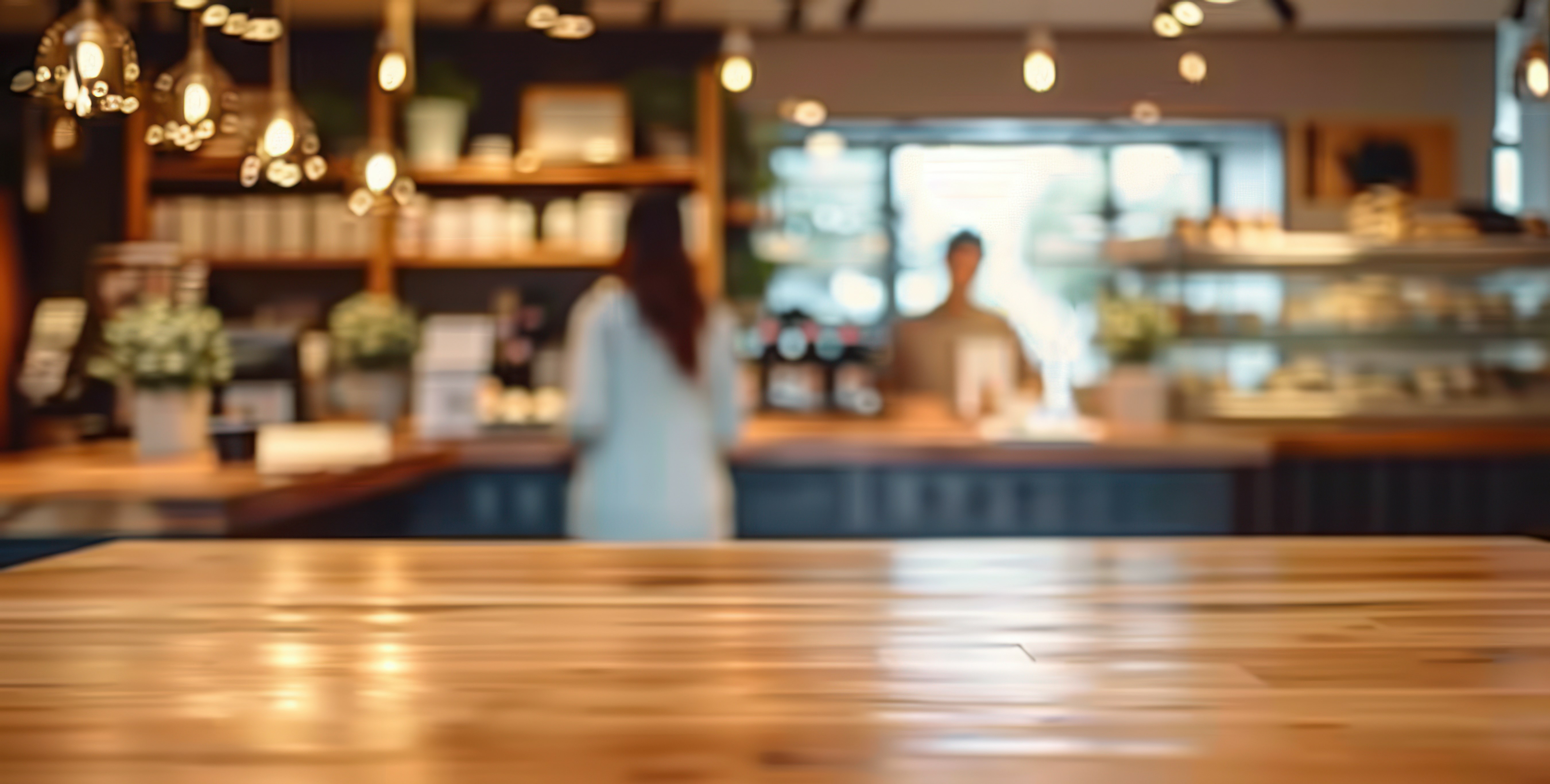 Wooden table in cafe perfect for product placement, with blurred background of workers and customers in a retail space.