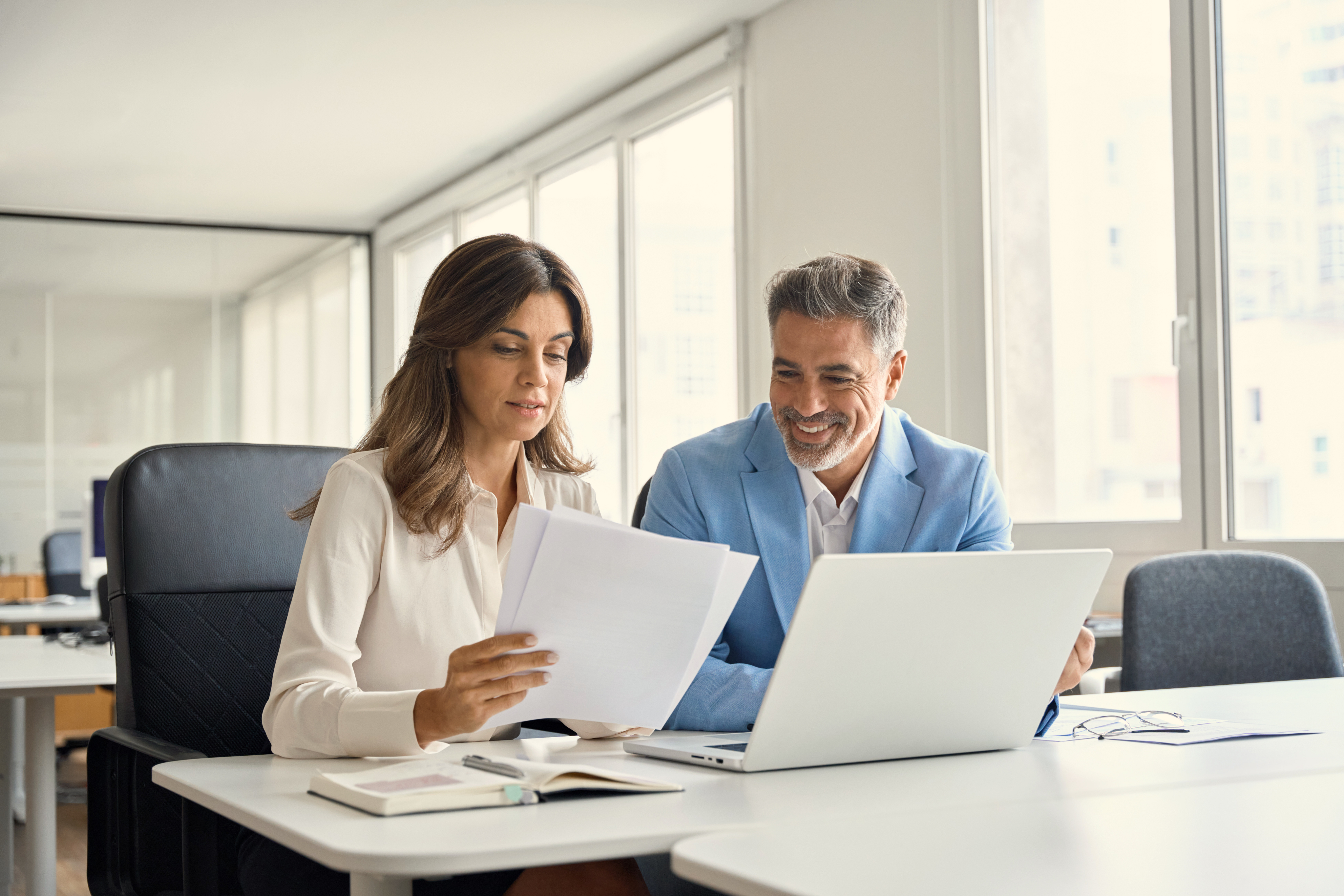 A man and woman reviewing documentation in an office building while looking at a computer.