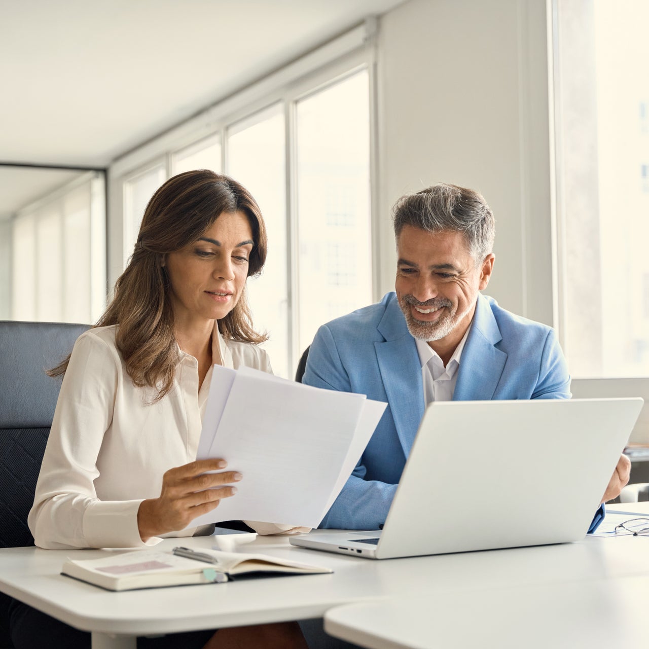 A man and woman reviewing documentation in an office building while looking at a computer.