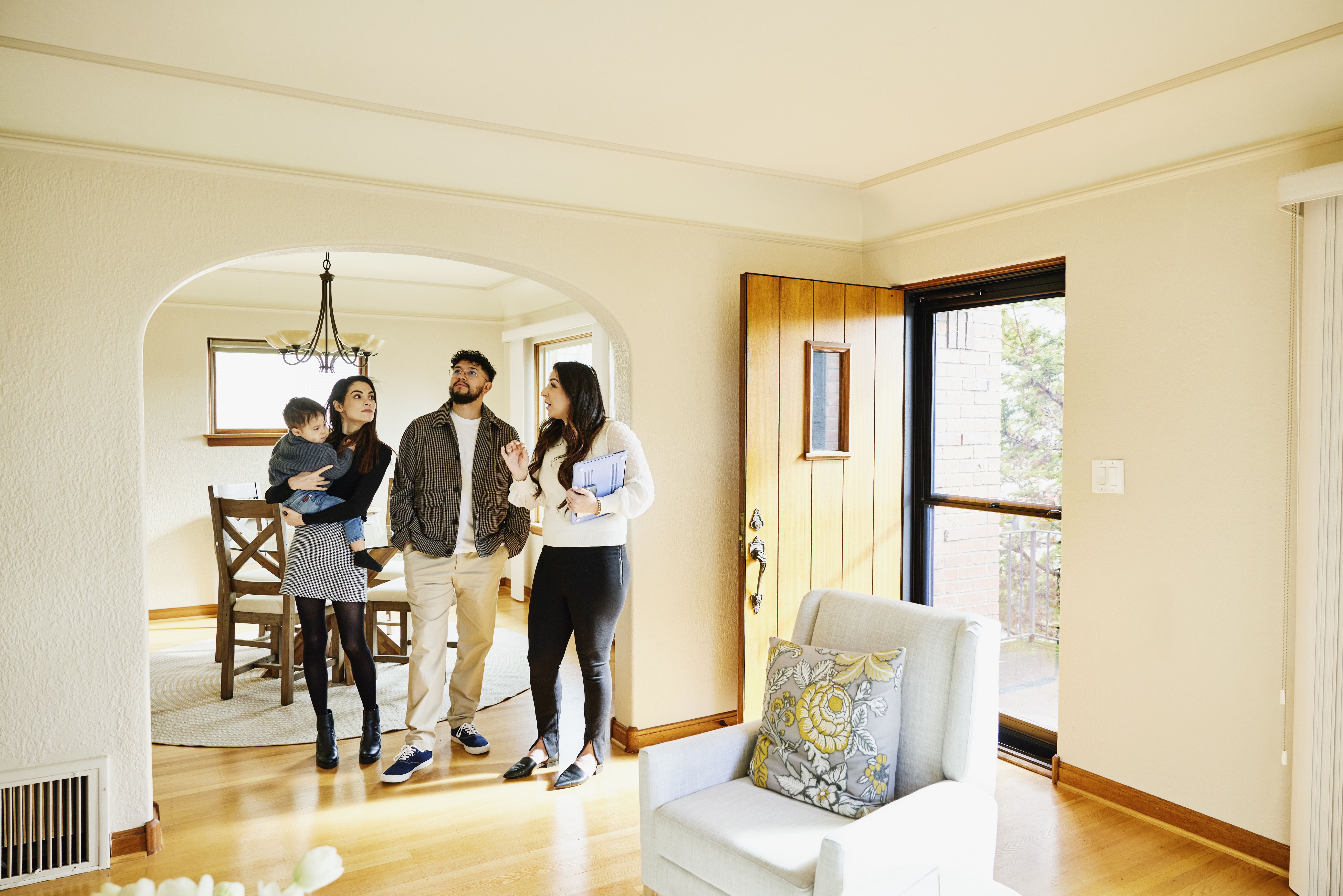 A family of three, including a baby, being shown a house by a real estate agent.
