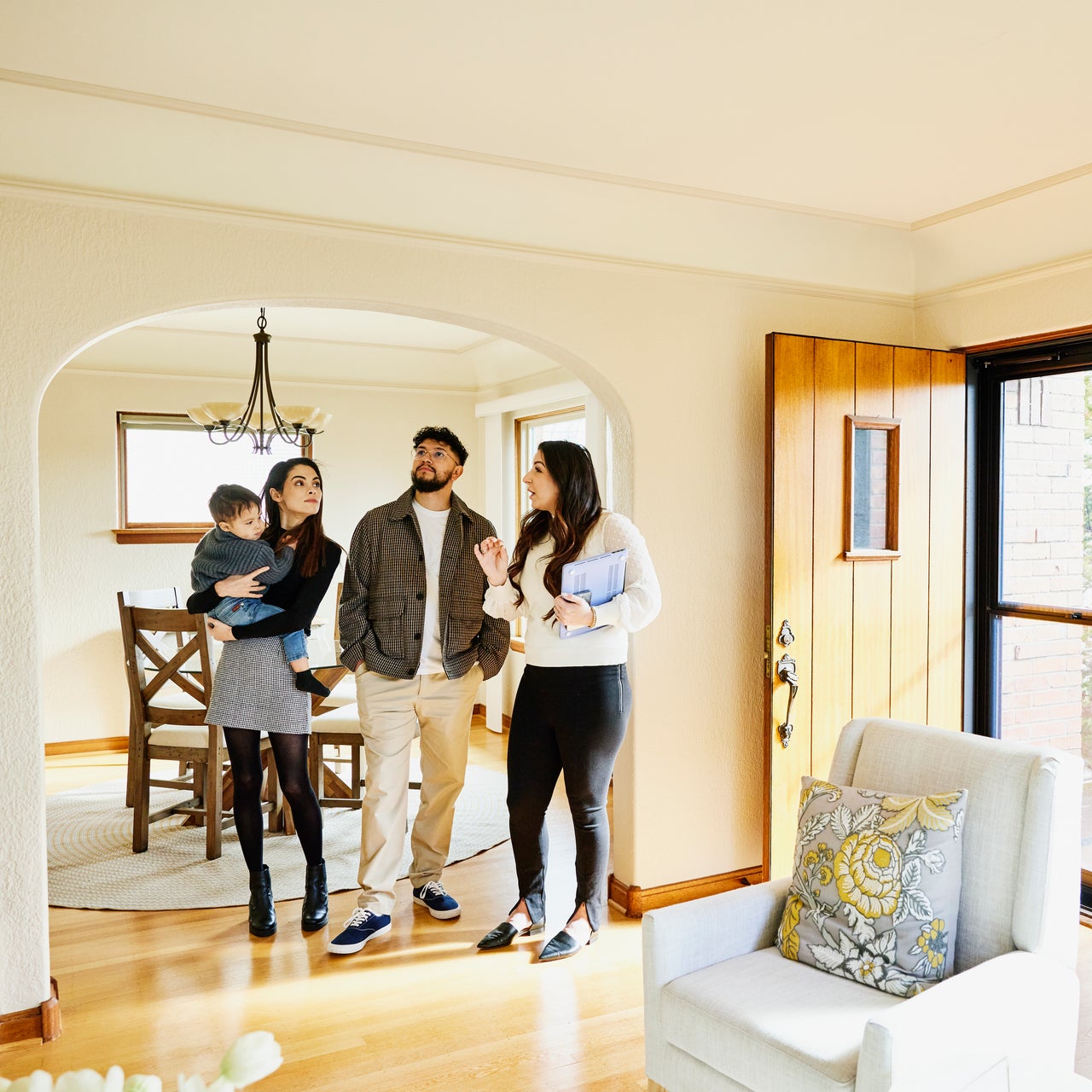 A family of three, including a baby, being shown a house by a real estate agent.