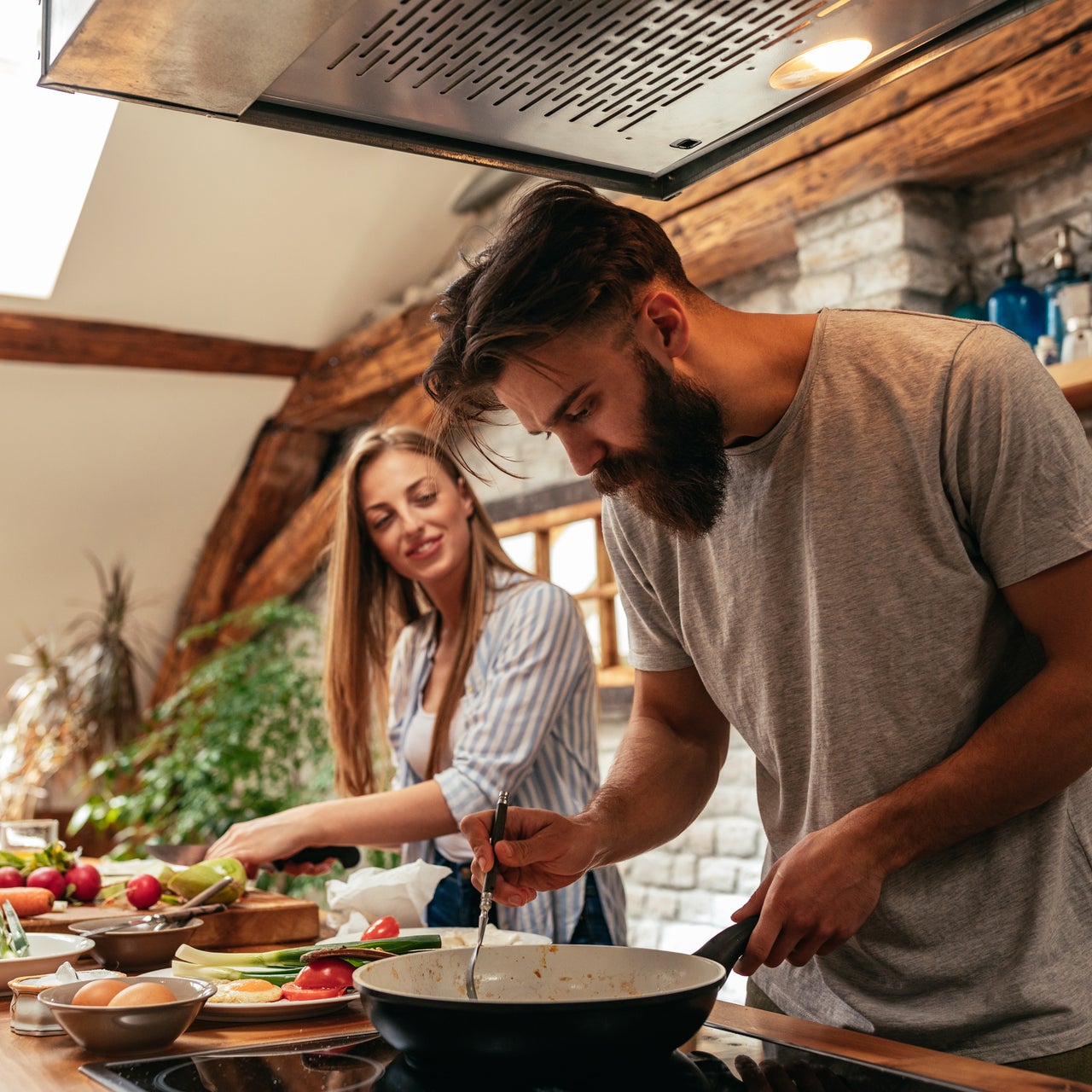 A couple cooking together in the kitchen. They are smiling.