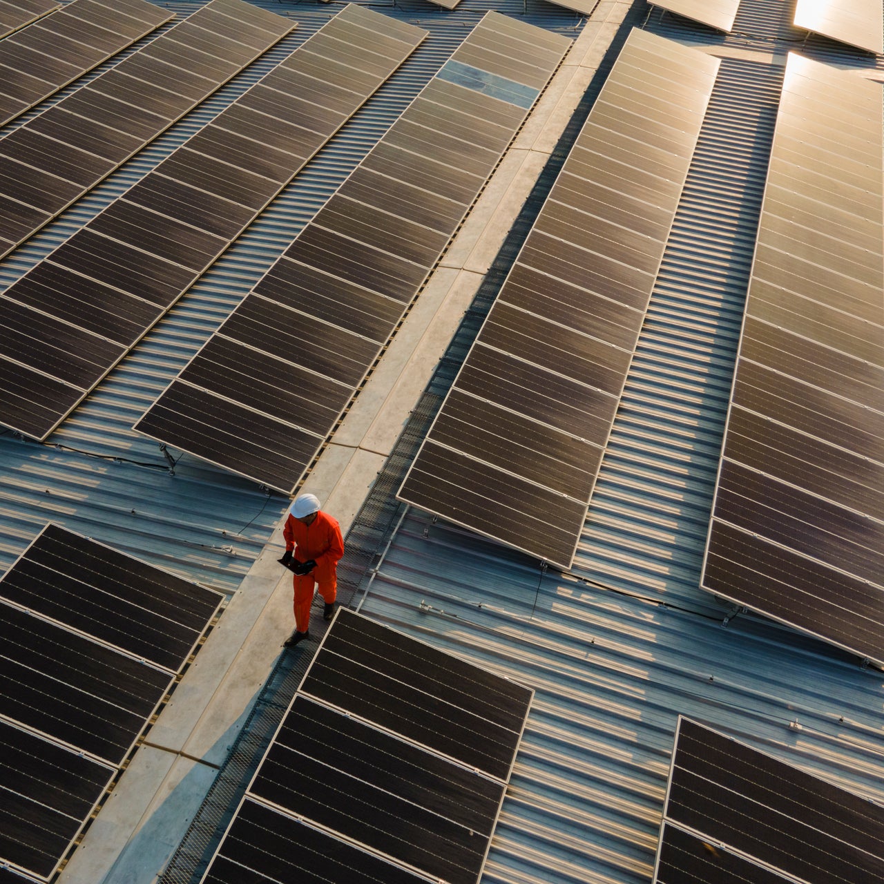 A view of numerous solar panels on the top of a property. An engineer is seen walking through it.