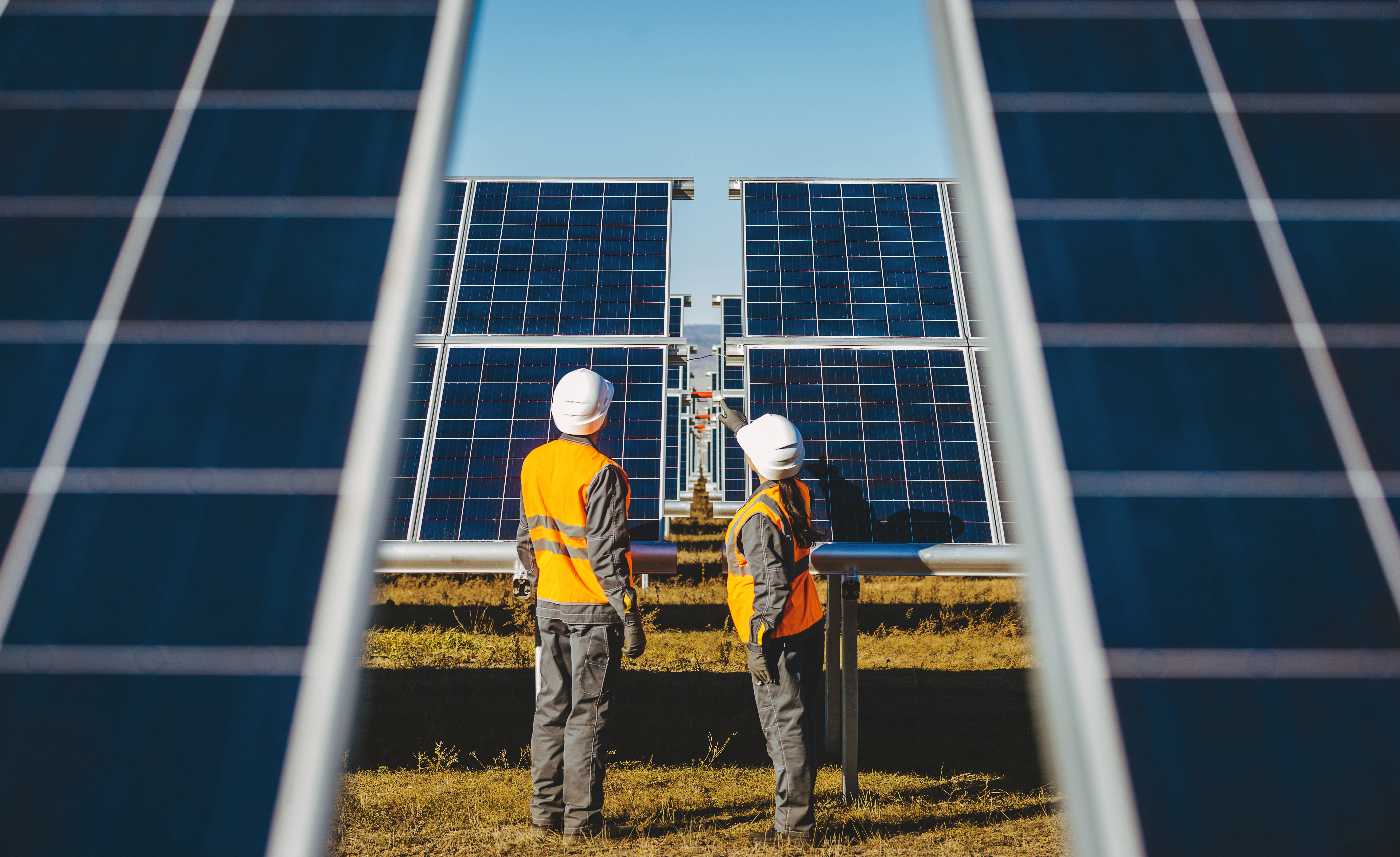 A view of numerous solar panels on the top of a property. An engineer is seen walking through it.