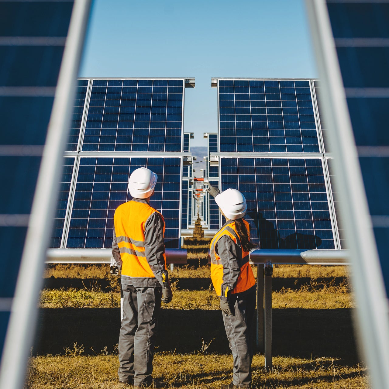 A view of numerous solar panels on the top of a property. An engineer is seen walking through it.