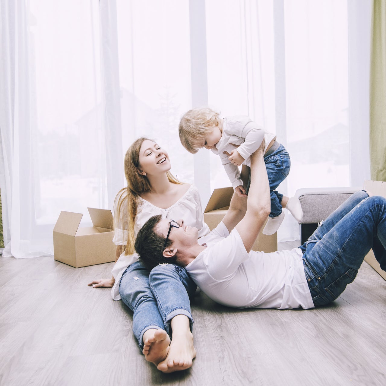 Two parents playing with their child in their new house with moving boxes.