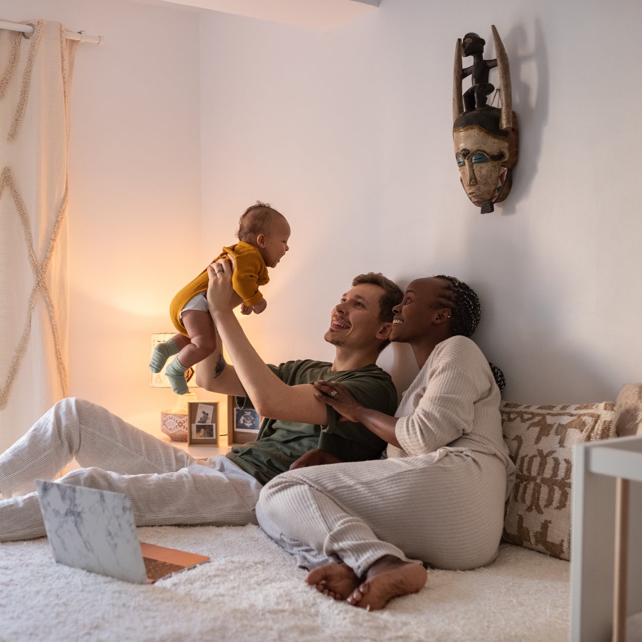 A young couple playing with their infant in their well organized and well lit bedroom.