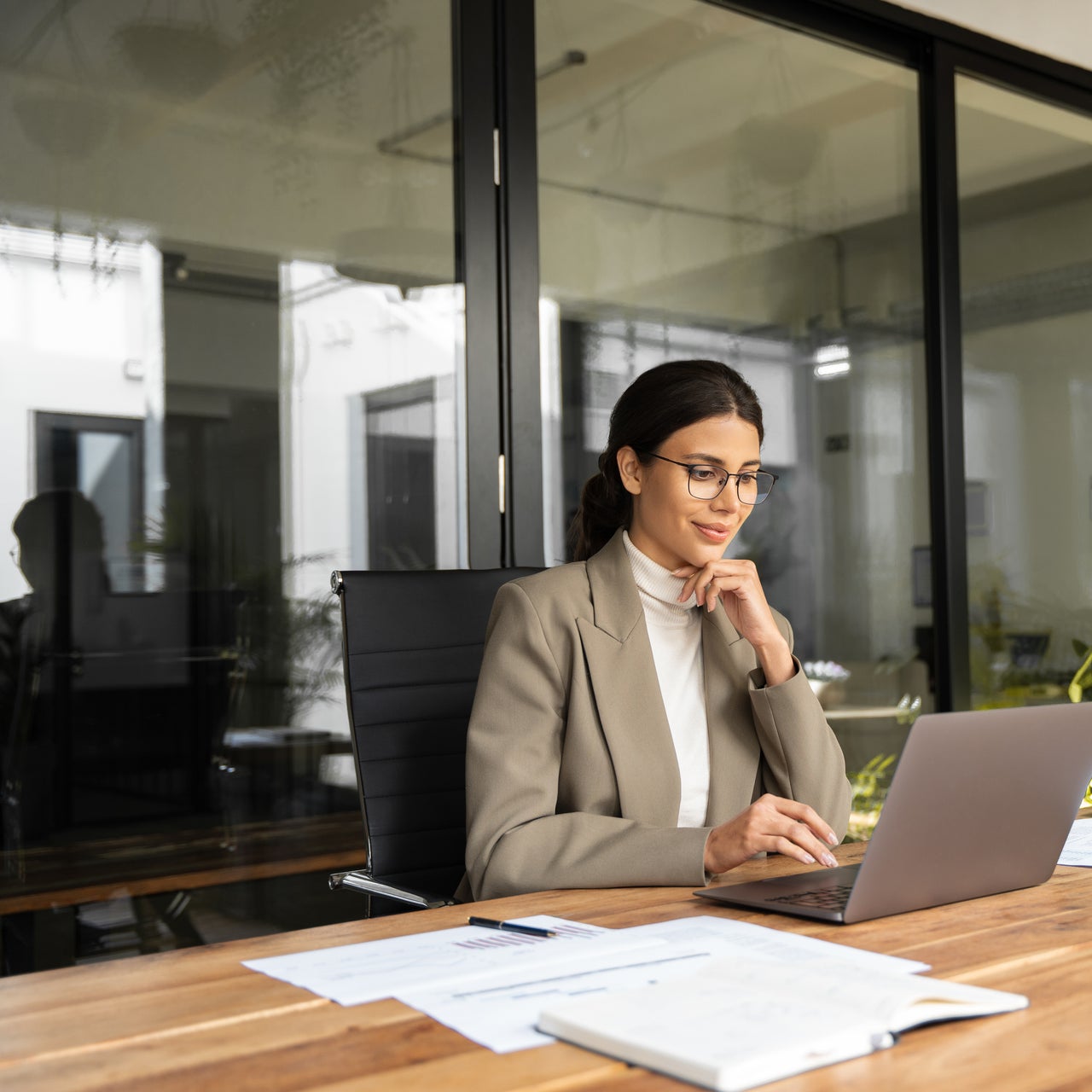 Businesswoman sitting in a modern office looking at an open laptop.