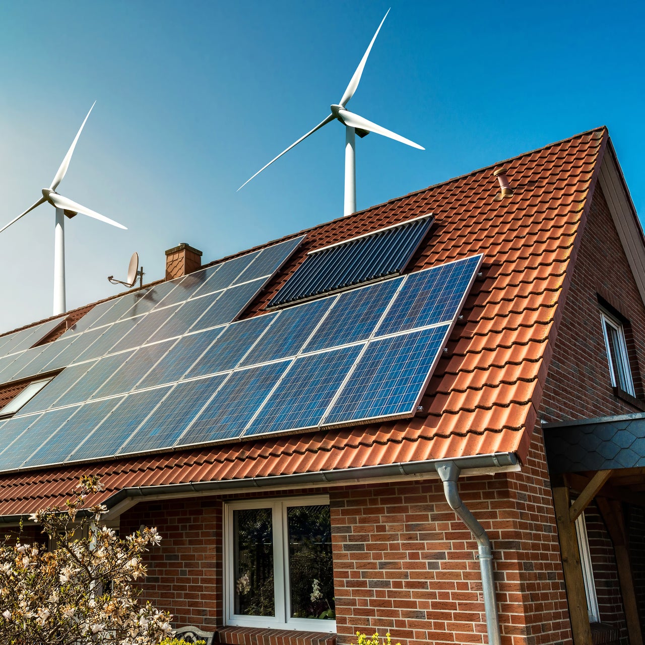 Solar panels are visible on the top of a residential property. There are also three wind mills around the house.