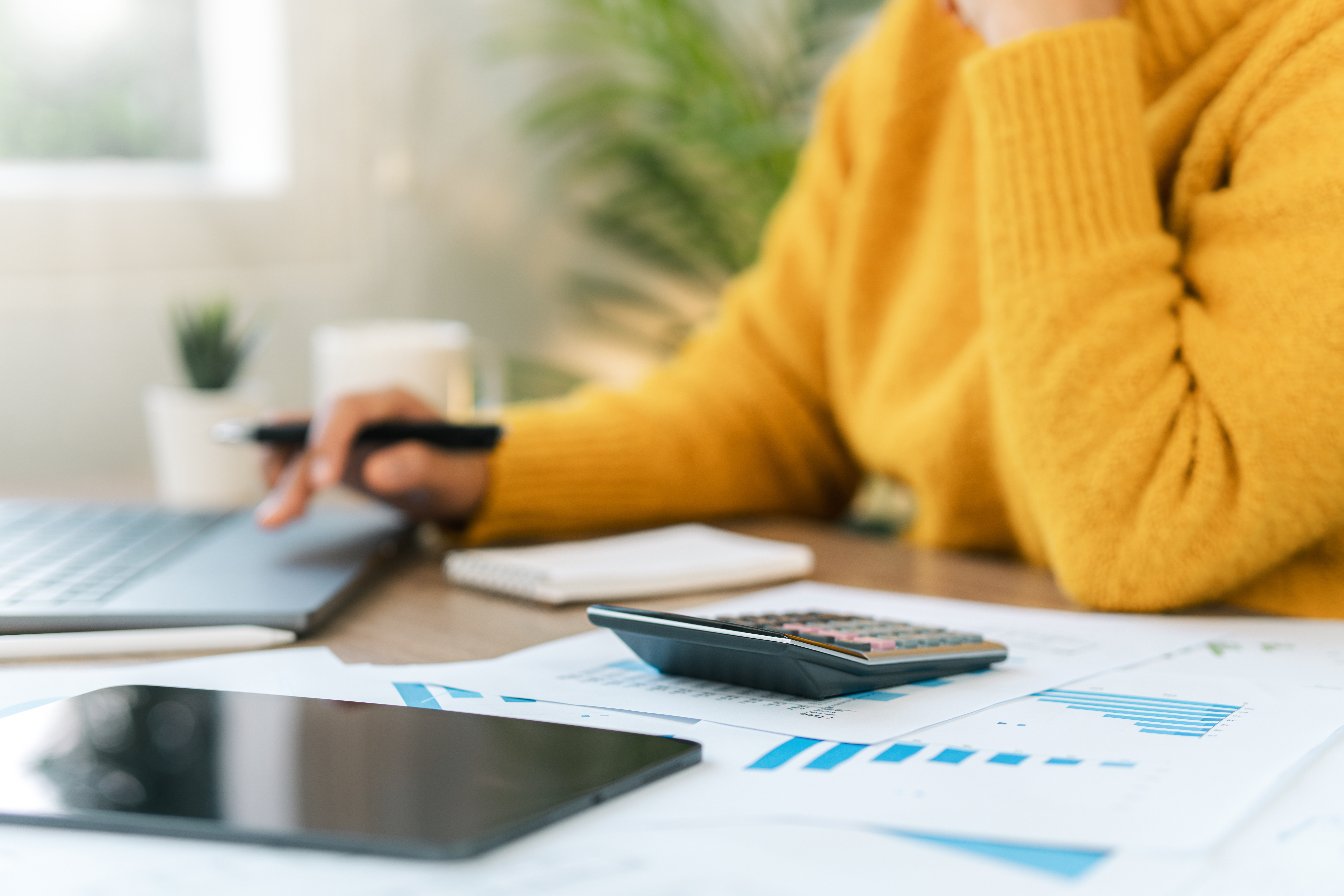 A person working on a laptop kept on a desk full of papers and a calculator.