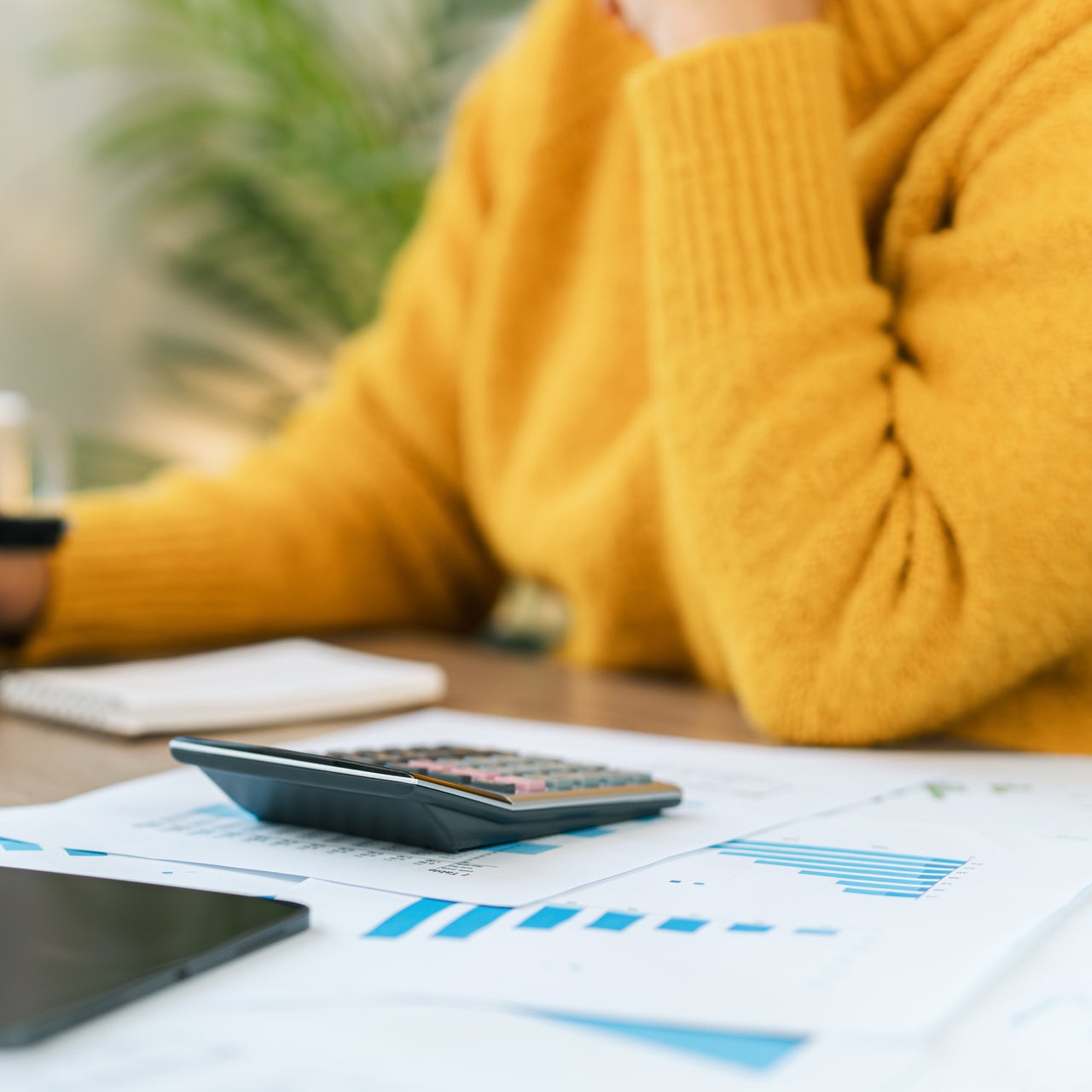 A person working on a laptop kept on a desk full of papers and a calculator.