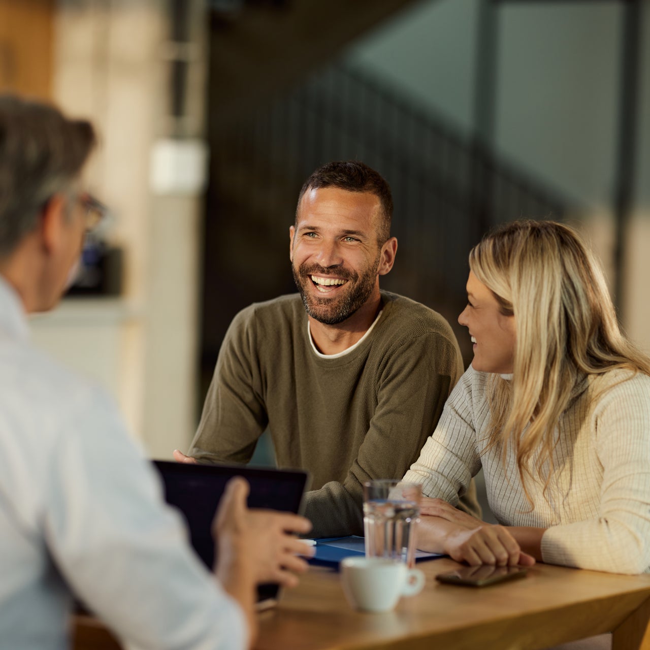 A smiling couple sitting with a man and discussing something over coffee.