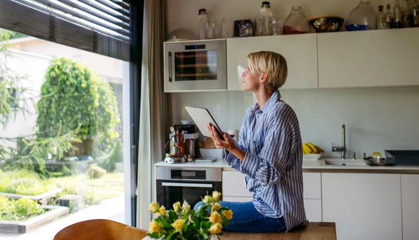 woman holding a tablet, looking out window.