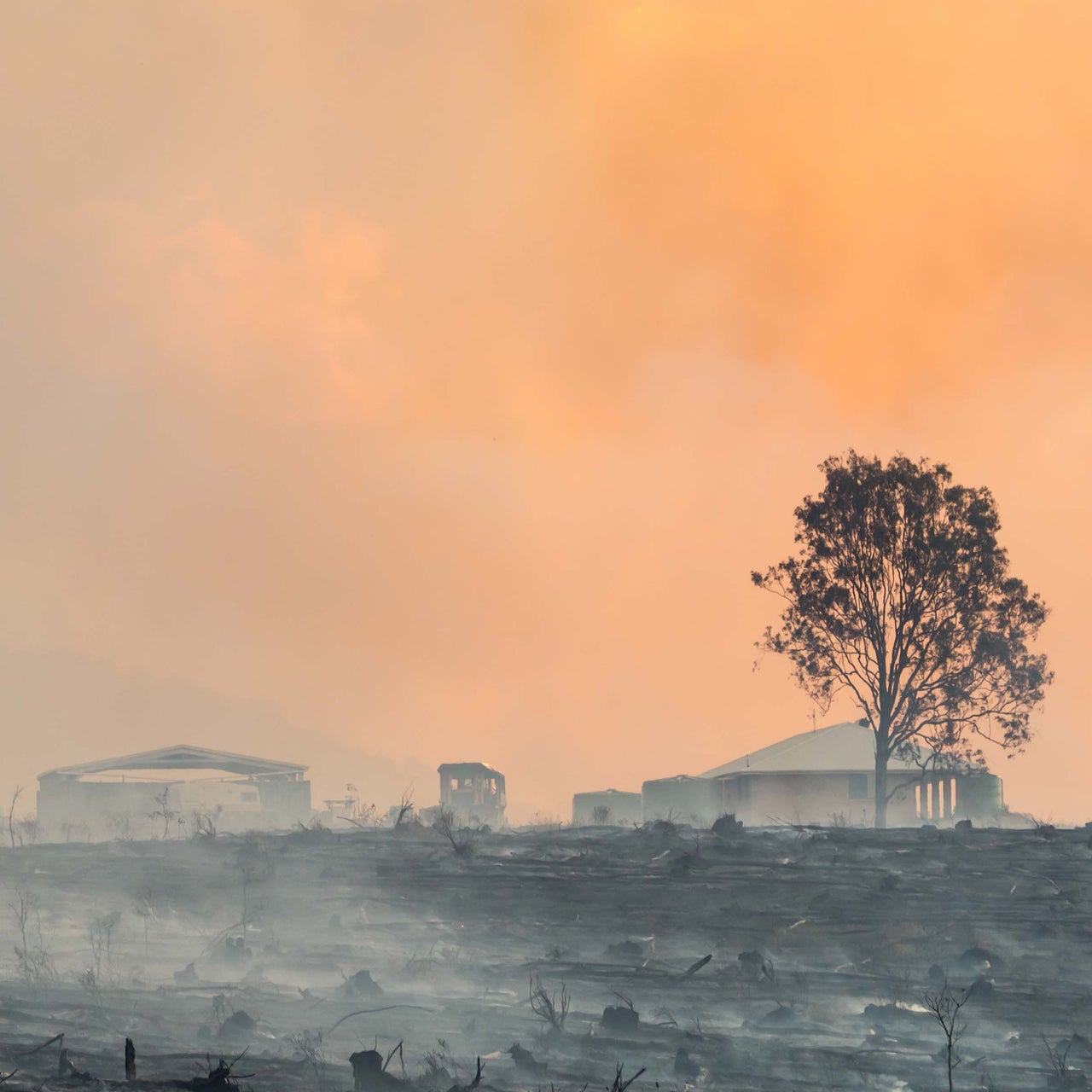 Row of houses on a hill with smoke rising in the background, indicating a possible wildfire hazard.