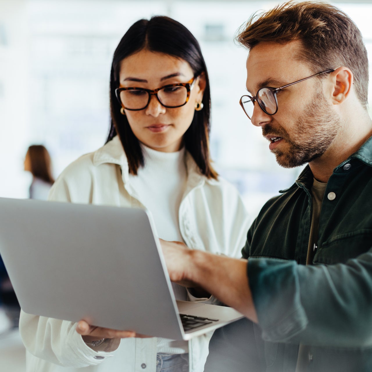 Two professionals are seen discussing something holding their laptop in hand.