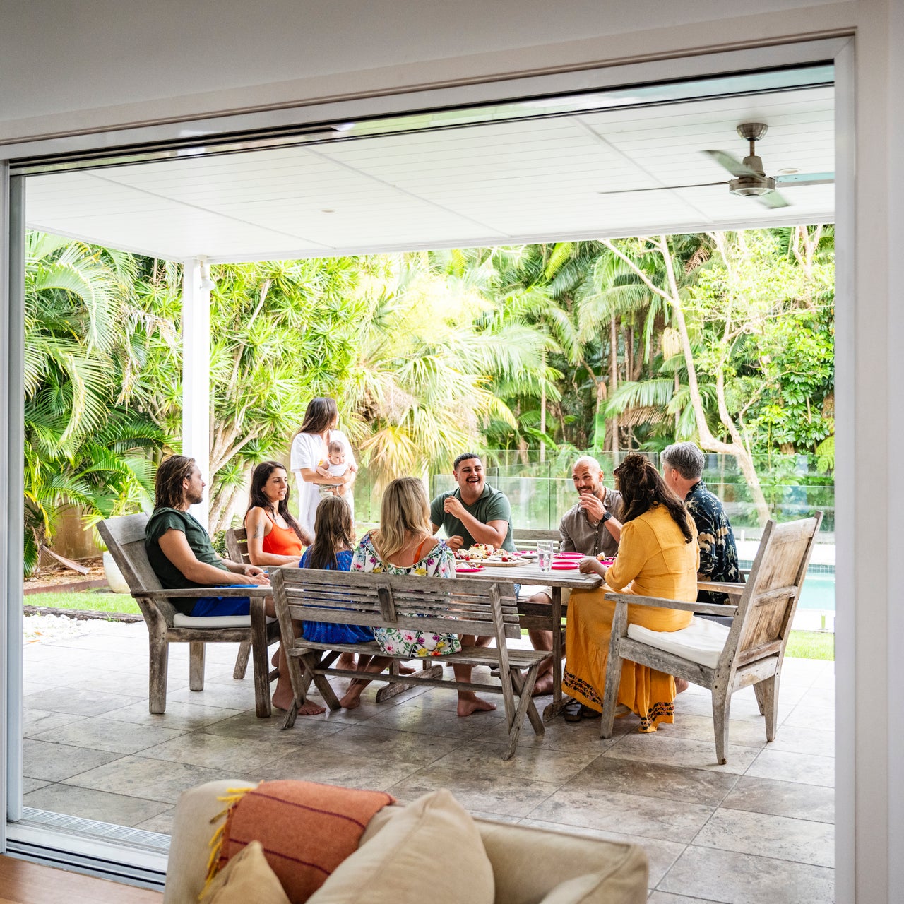 Group of people sitting around a table on an outdoor patio surrounded by lush greenery, enjoying a social afternoon..