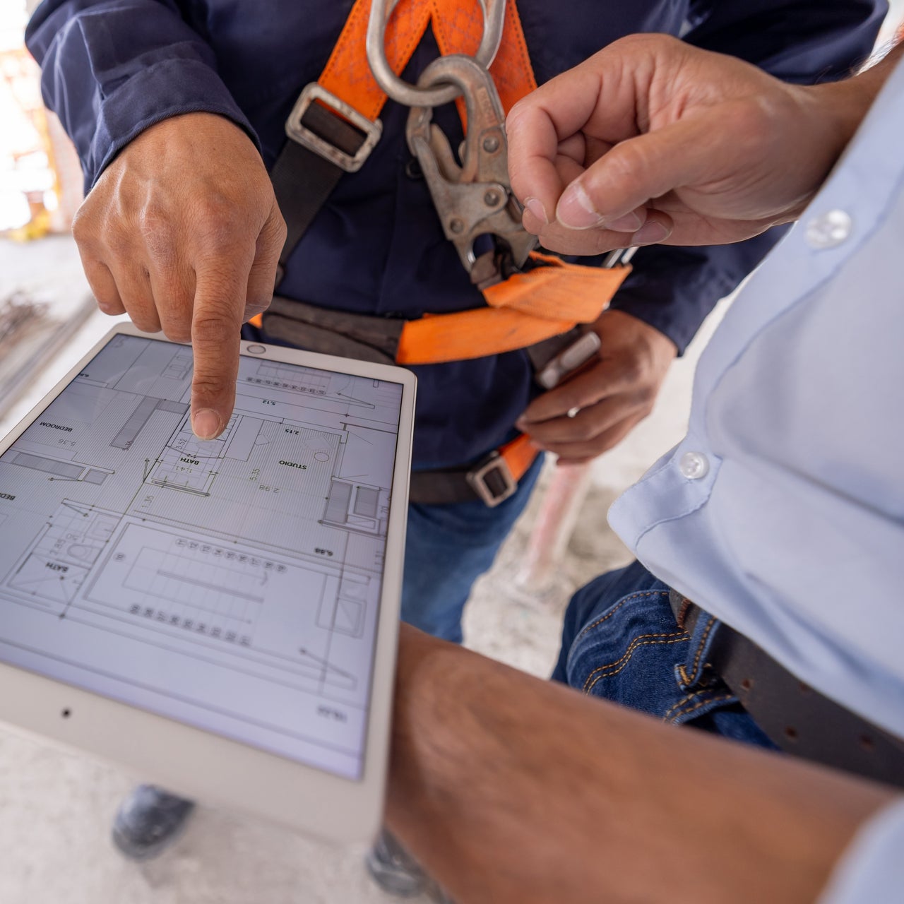 Two construction workers are reviewing a building plan on a tablet.