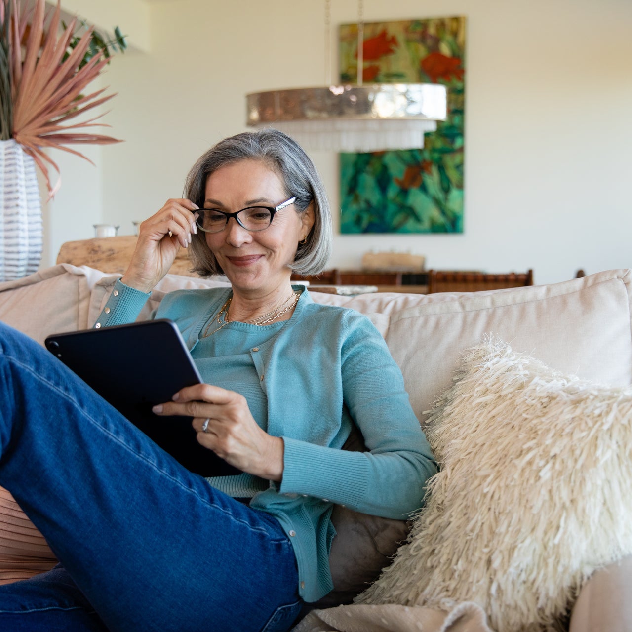 An elderly woman is looking into her tablet in a relaxed mood on her couch.