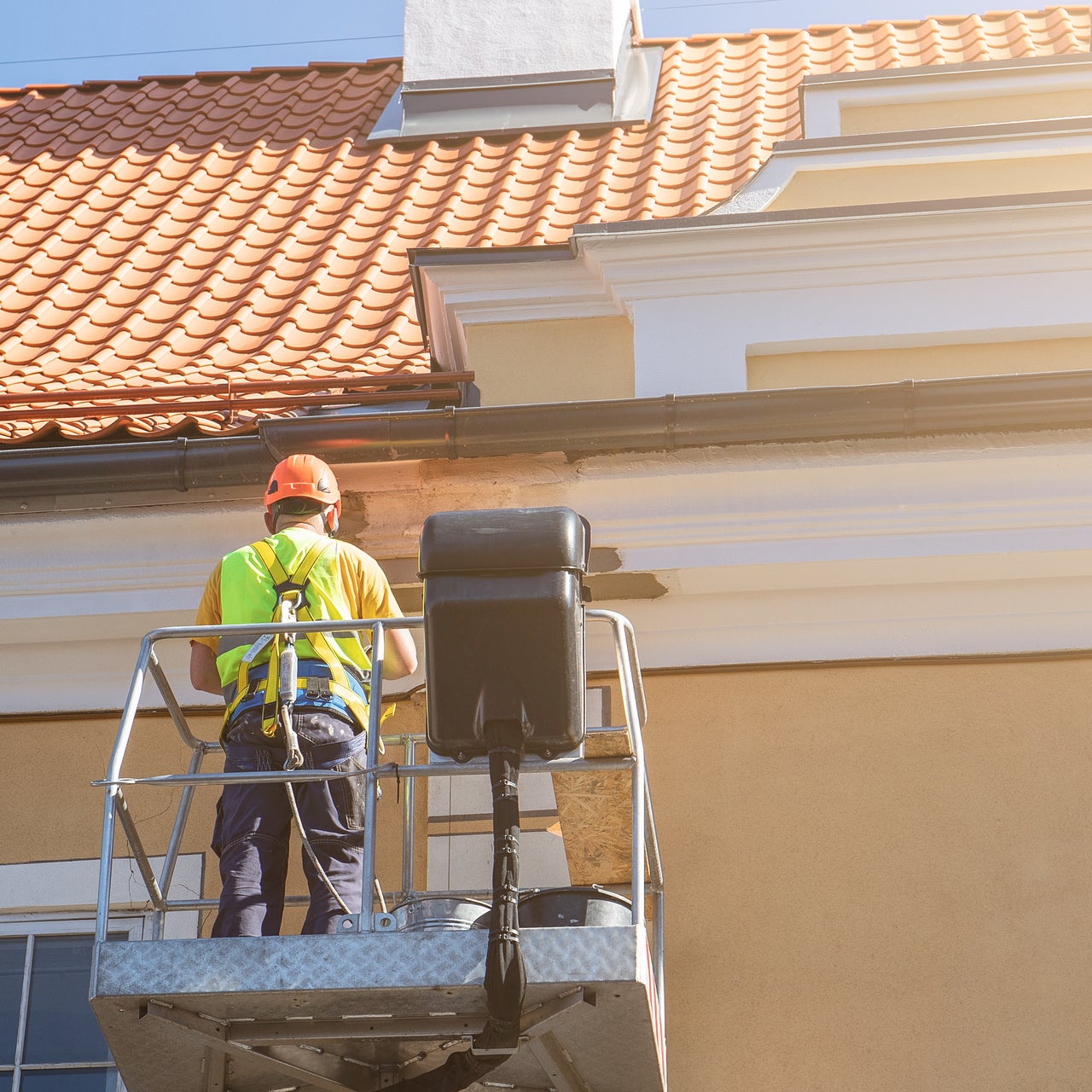 A construction worker is seen on a lift, likely involved in roof painting or maintenance.
