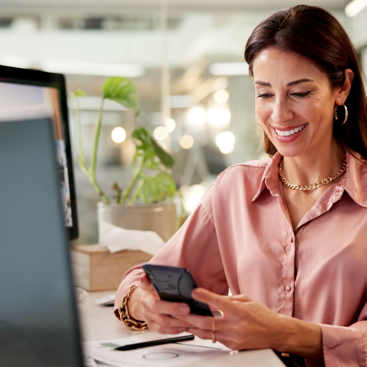 A woman sitting on a chair and looking at her phone, smiling.