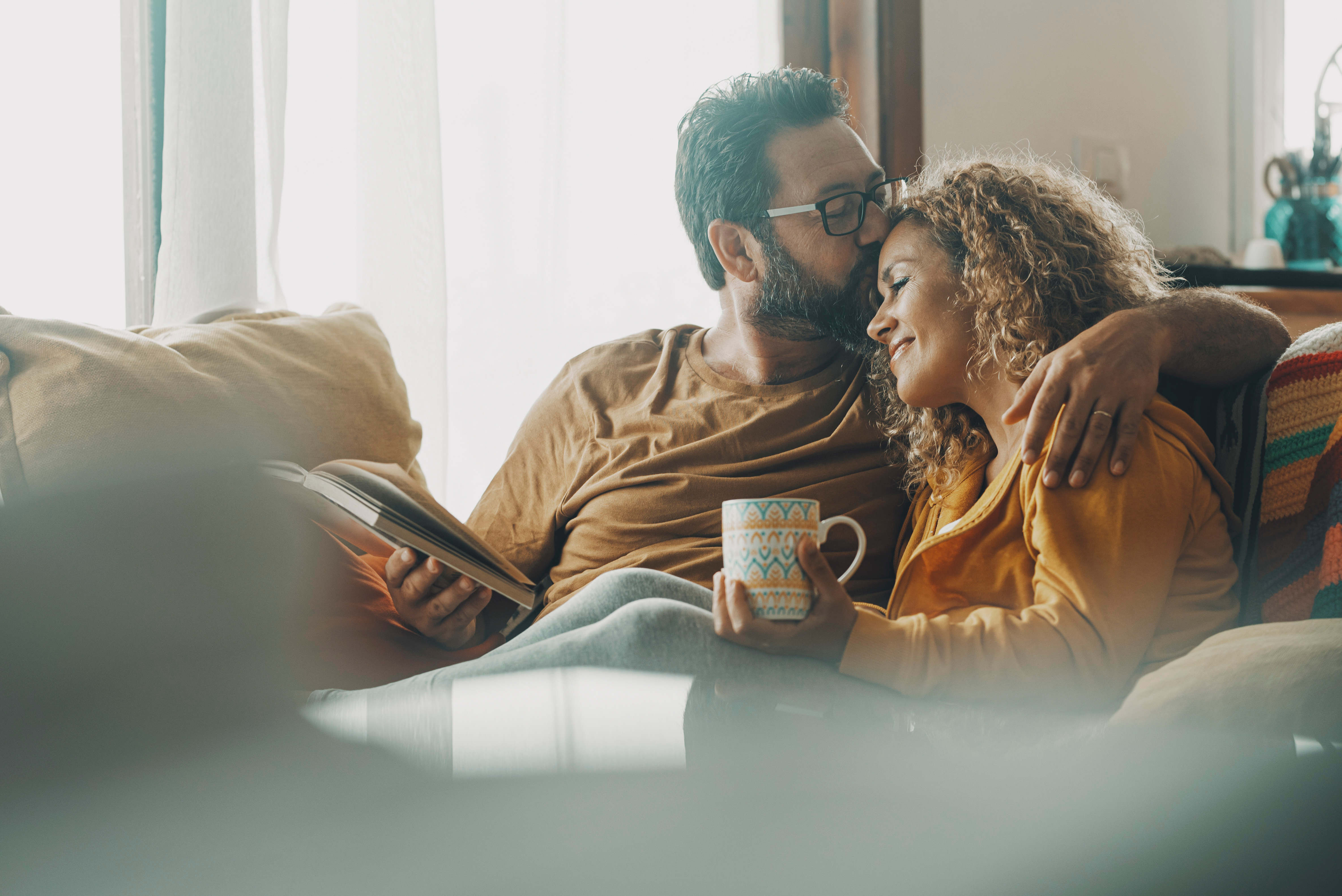 A man kissing a woman on the forehead. They are sitting together on a couch. 