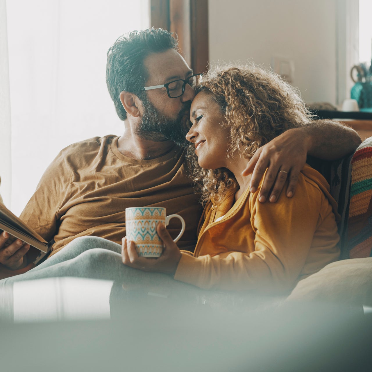 A man kissing a woman on the forehead. They are sitting together on a couch.
