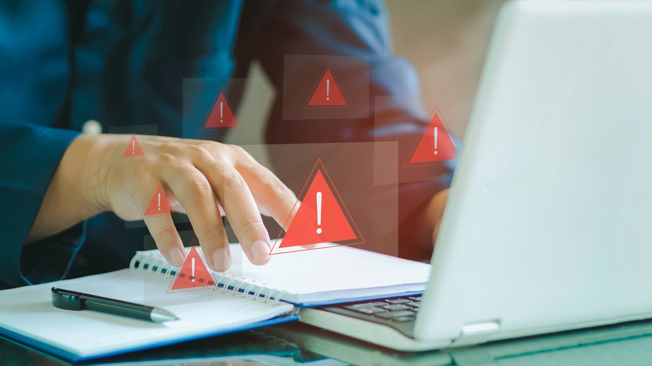 An image of someone on their laptop and several warning signals popping up highlighting an urgent data breach