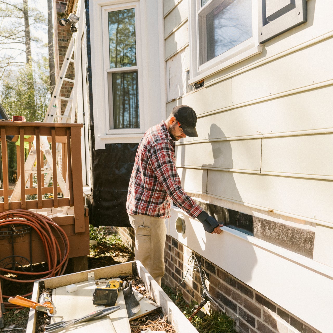 A man is shown working on the siding of a house. He appears to be installing or repairing the siding.