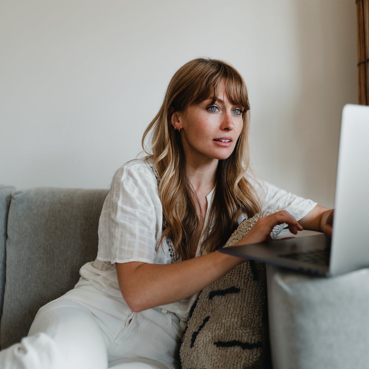 A young woman is seen working on a laptop, sitting on a sofa.