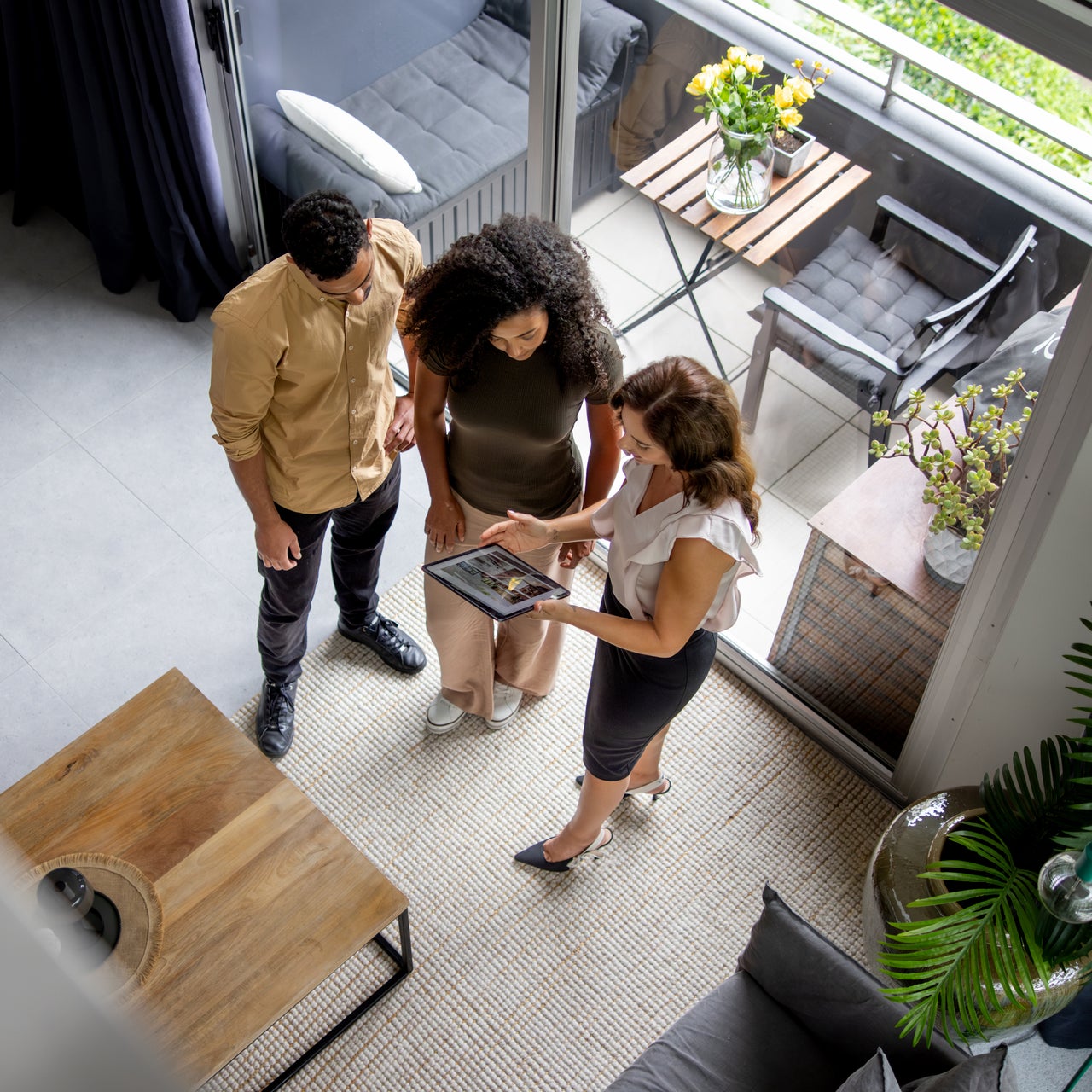 A real estate agent is seen showing a couple a property on a tablet, standing in a modern apartment.