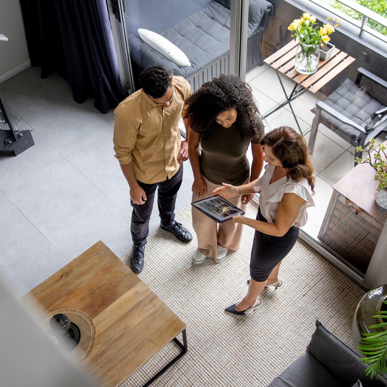 Three people stand outside a modern house, with one person holding a tablet and gesturing, discussing property details.