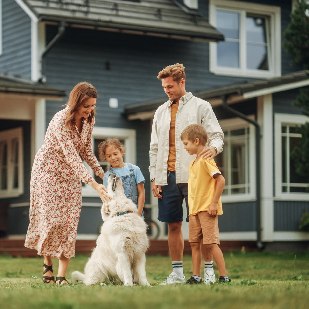 A couple and their two children are playing with their pet dog in a outdoor area of their residence.