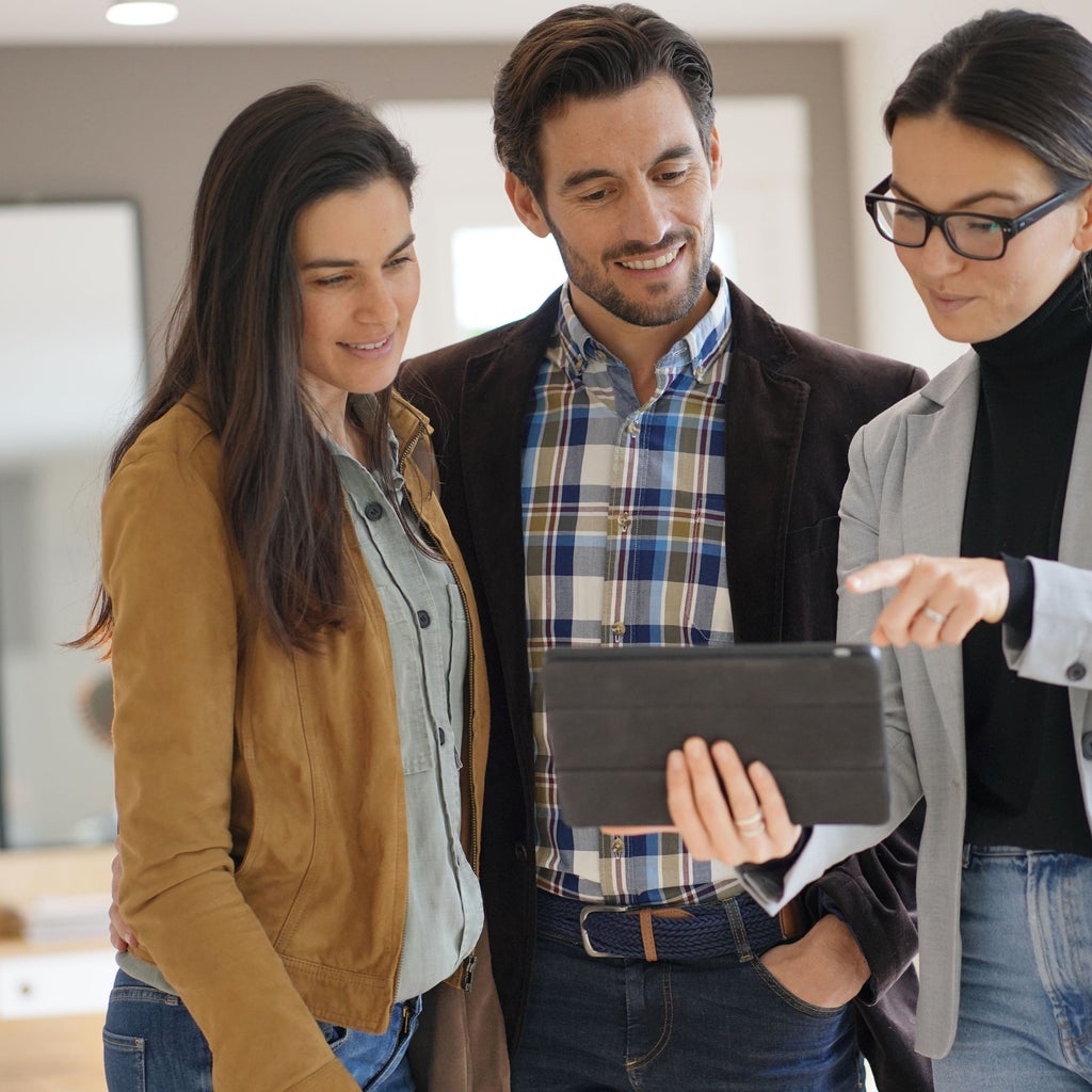 A woman professional showing something on her tablet screen to two other professionals, a man and woman. They are all smiling.