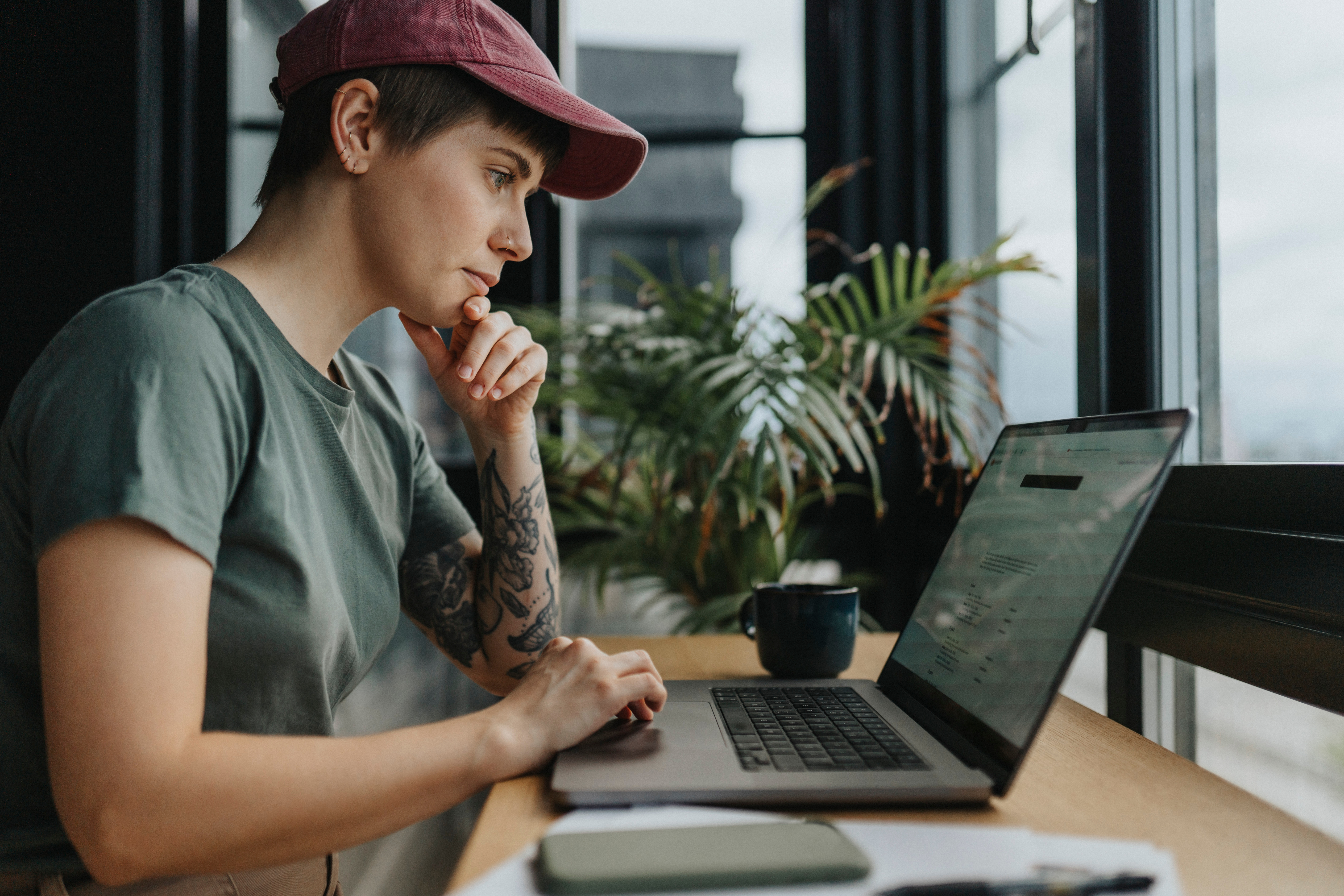 A woman is sitting on a chair and looking seriously into her laptop screen.