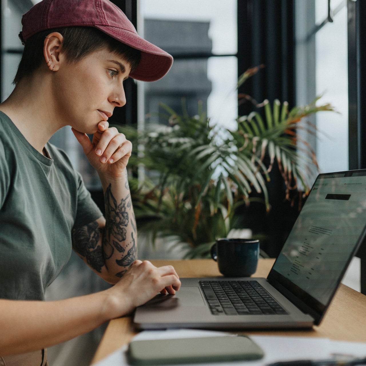 A woman is sitting on a chair and looking seriously into her laptop screen.
