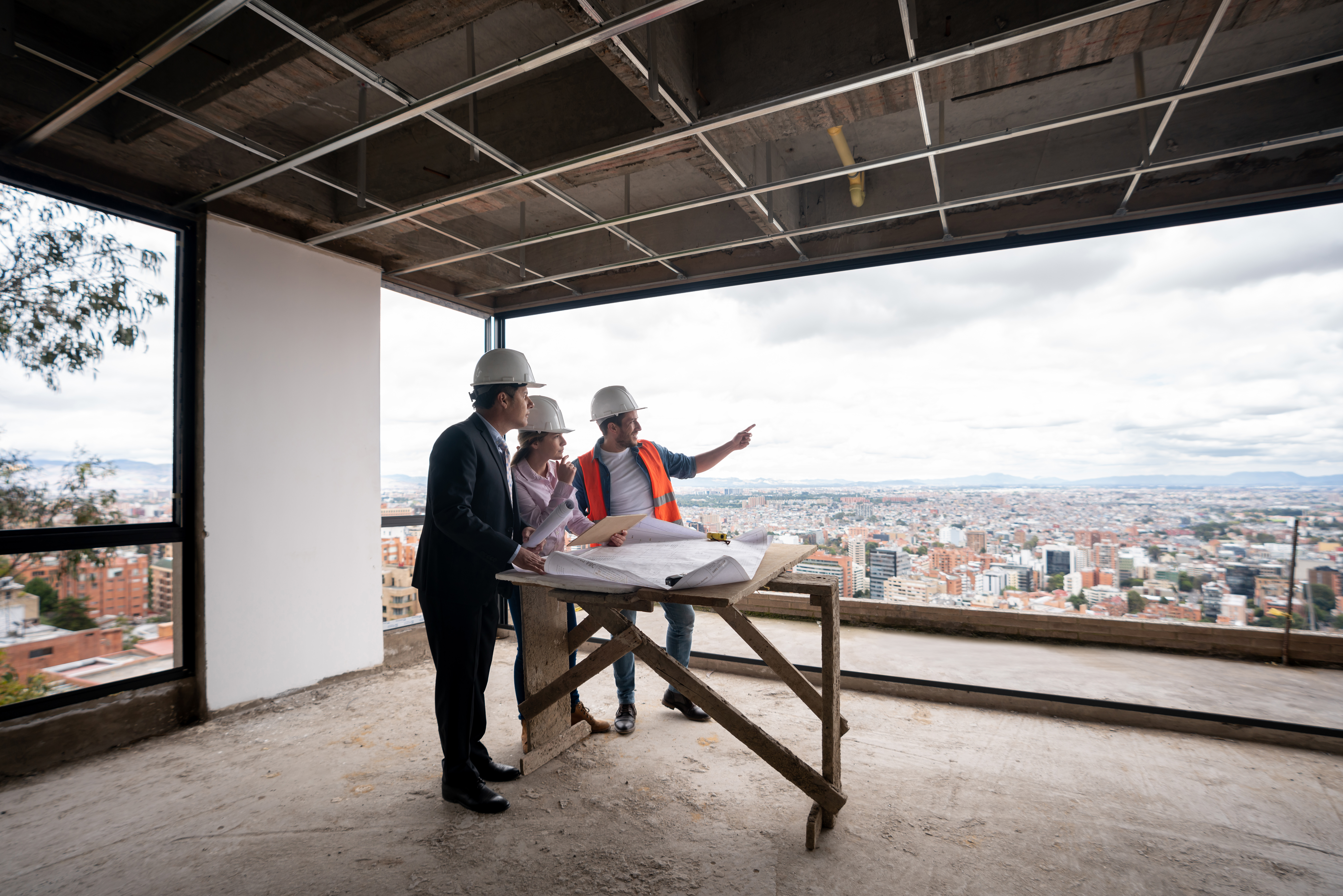 Contractor, architect and engineer working together as a team at a construction site and pointing at the windows while looking at a blueprint.