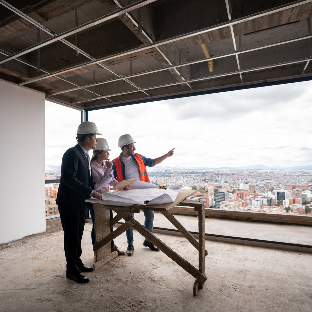 Contractor, architect and engineer working together as a team at a construction site and pointing at the windows while looking at a blueprint.