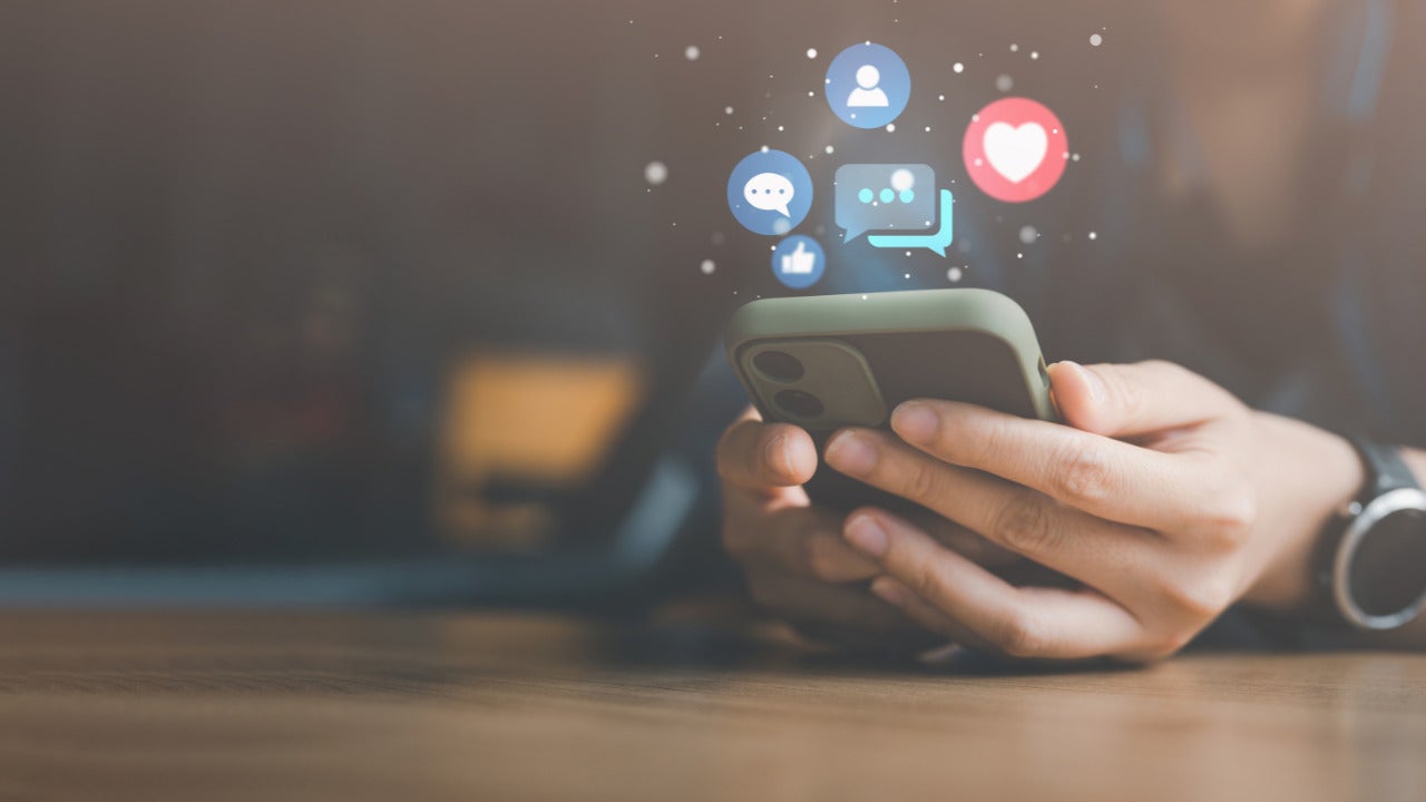 An illustration of social media icons hovering over a phone that a person is interacting with