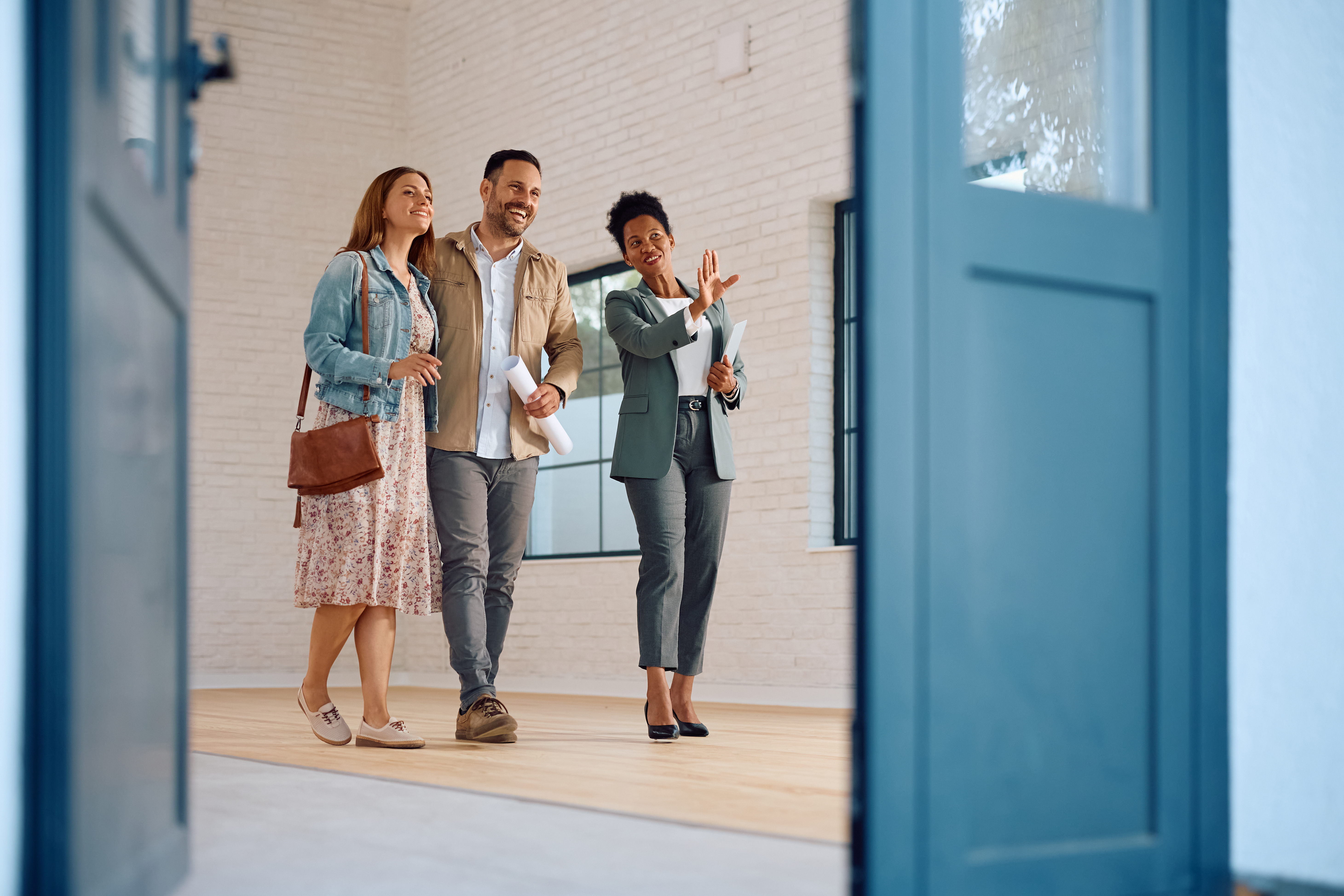 A real estate professional guiding a young couple through a new home. This represents the successful homeowner journey and the role of credit unions as trusted advisors.