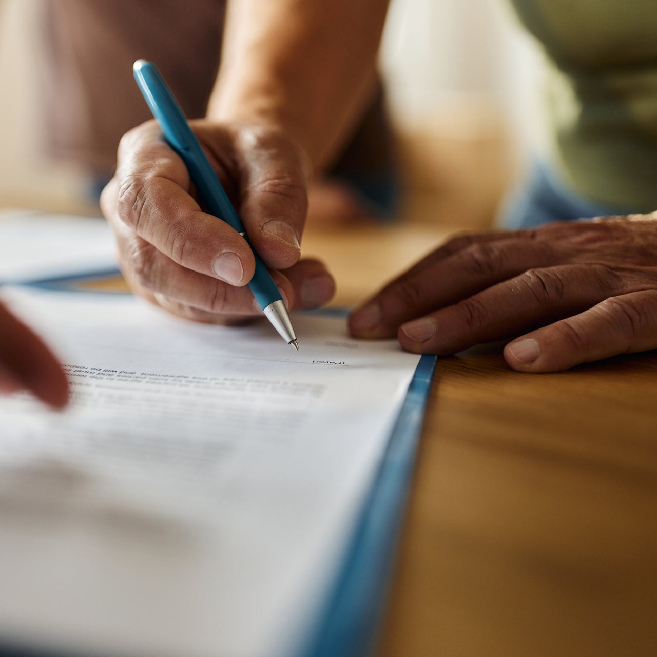 The image shows a person's hands signing a document with a blue pen.