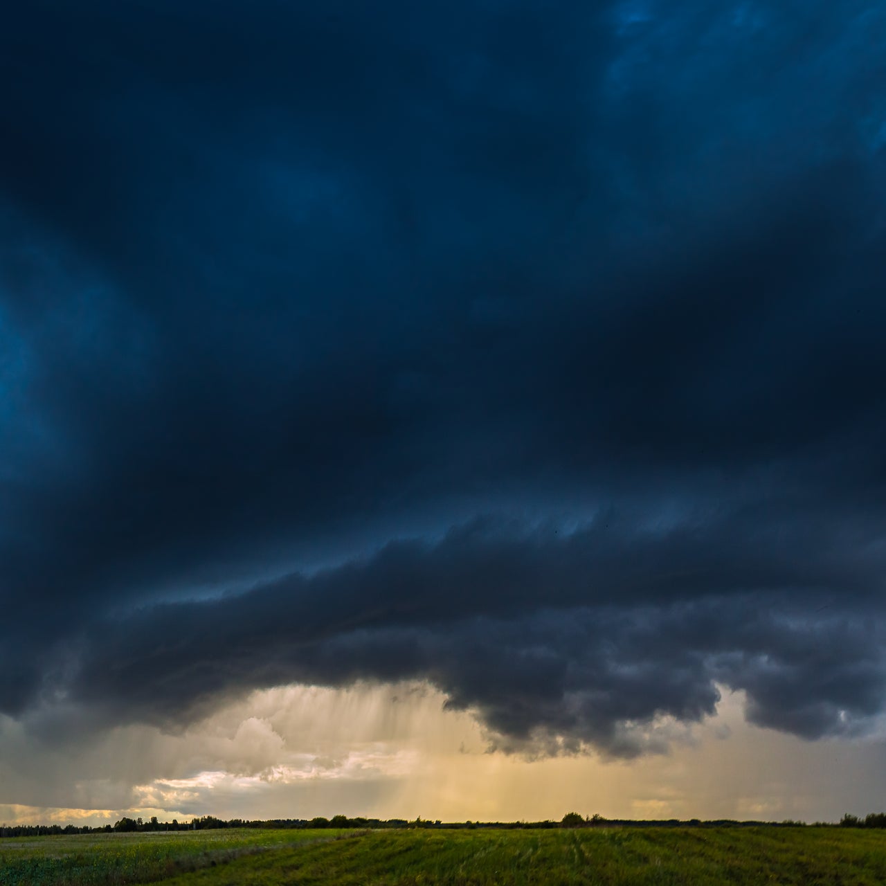 A stormy sky over a vast green field at dusk.