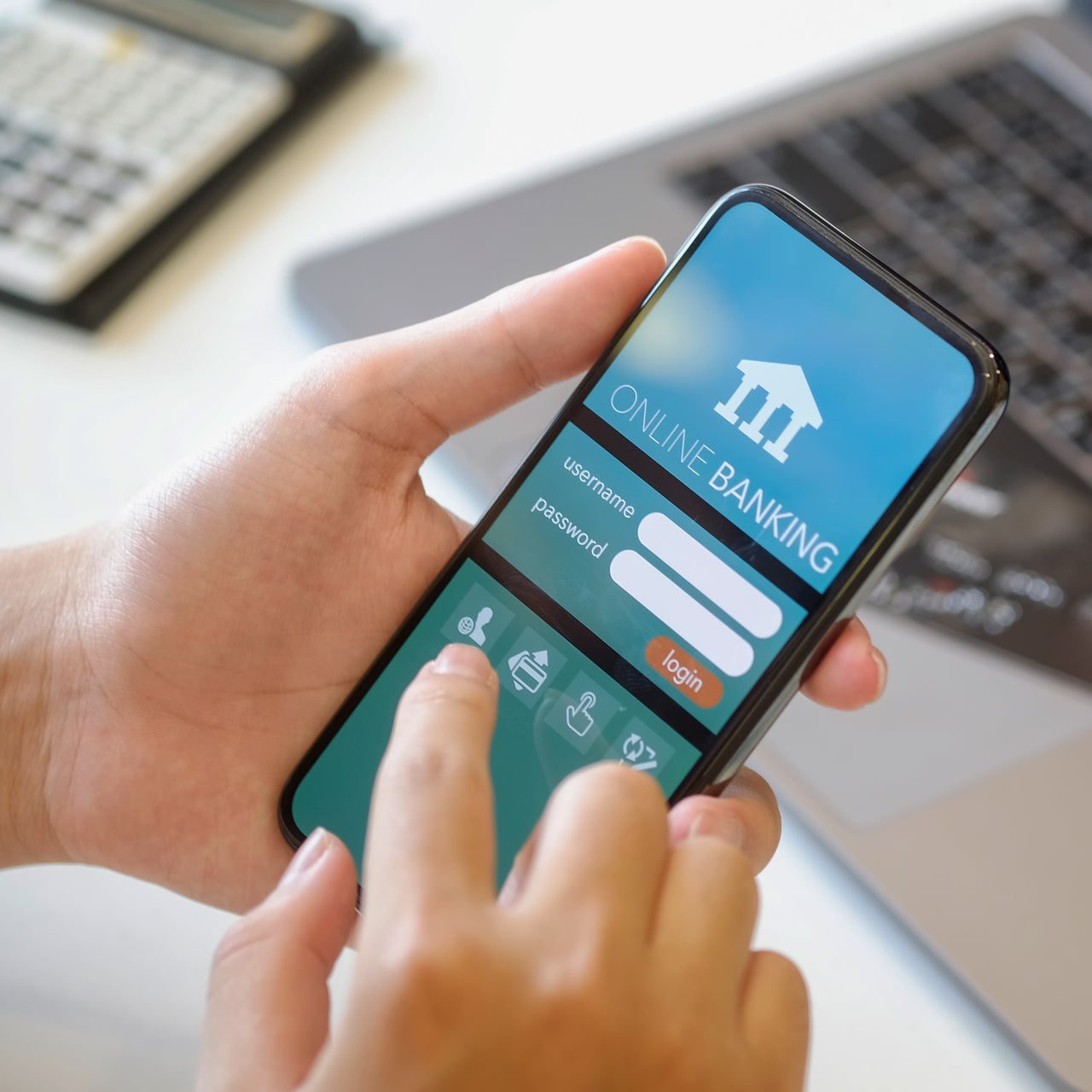 A hand is visible on a smartphone browsing through an online banking screen.